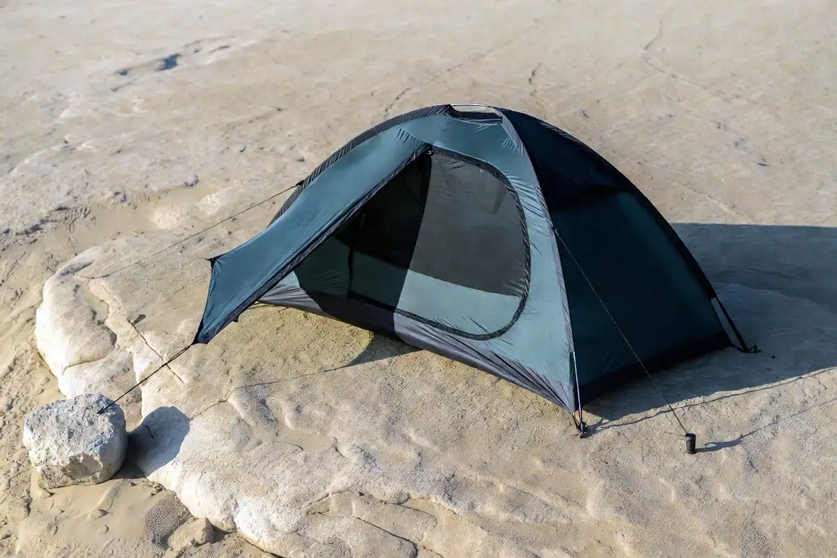 camper anchoring tent on rock and sand