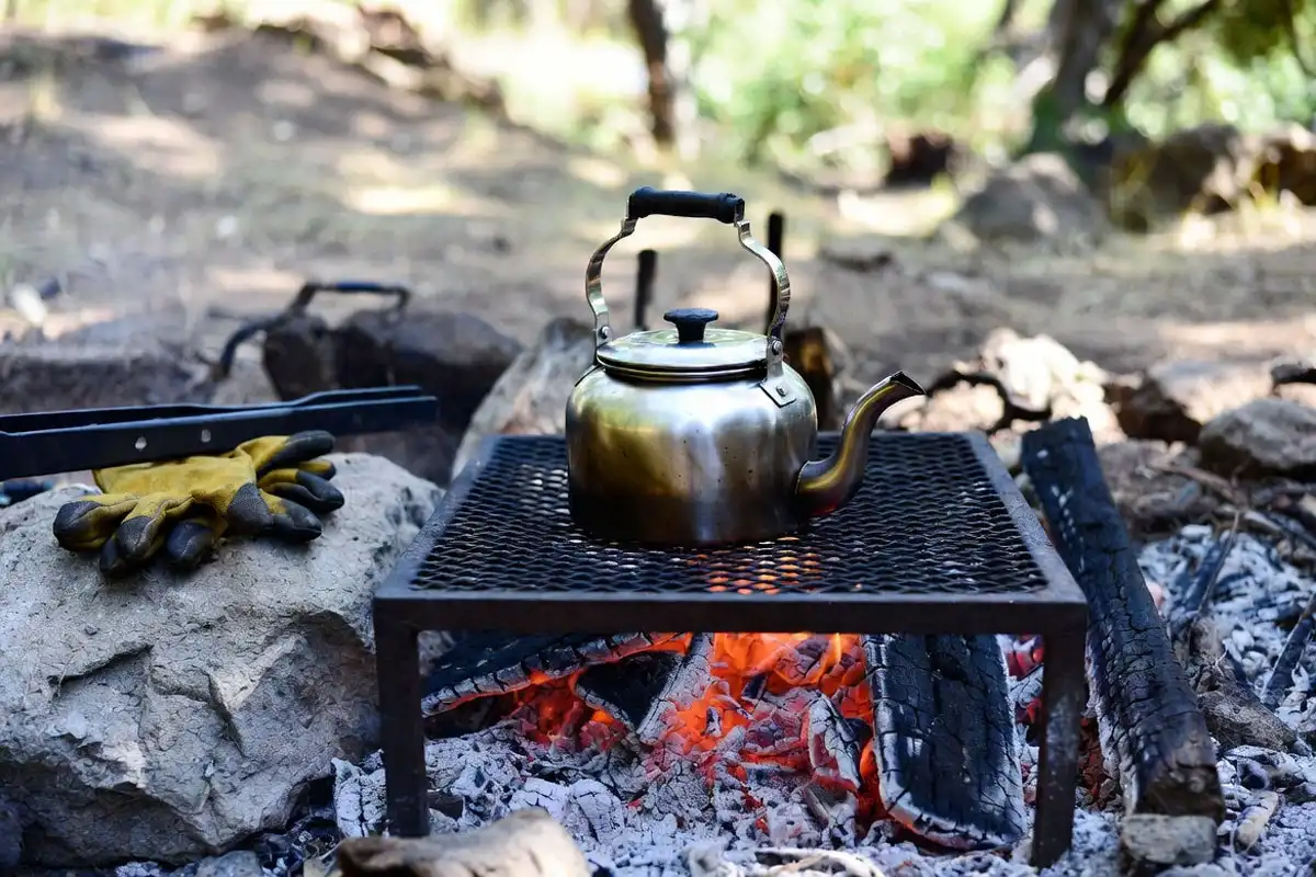 kettle on grate over coals with gloves nearby