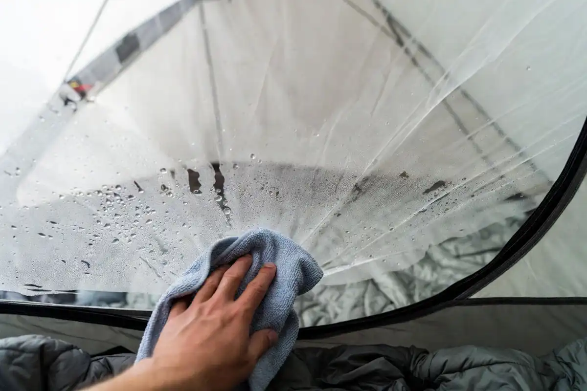 hand wiping tent wall condensation before droplets fall onto bedding