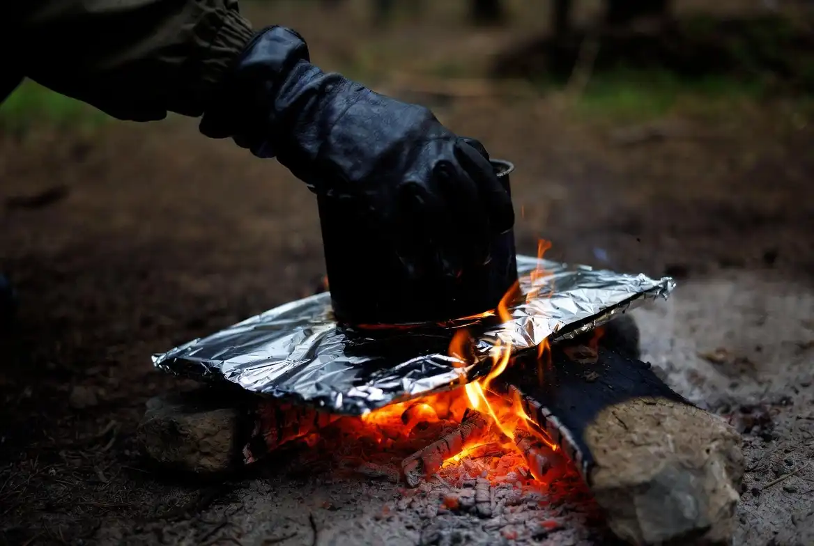 camper placing foil under camp pot over campfire coals
