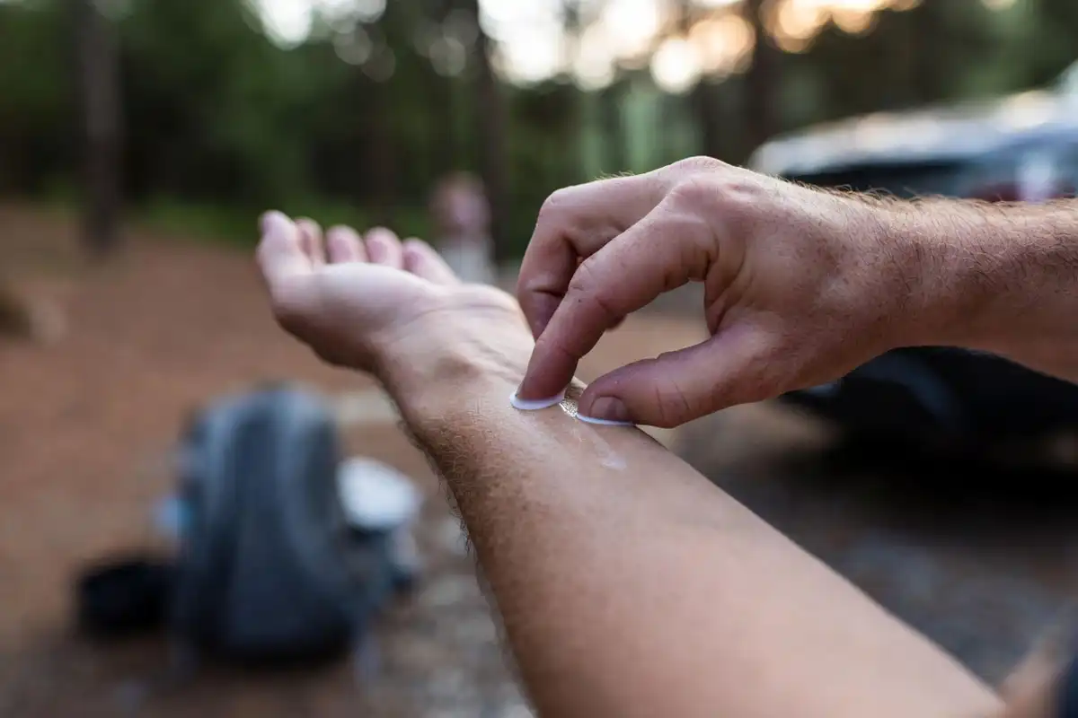 hiker rubbing insect repellent lotion on forearm before a forest hike