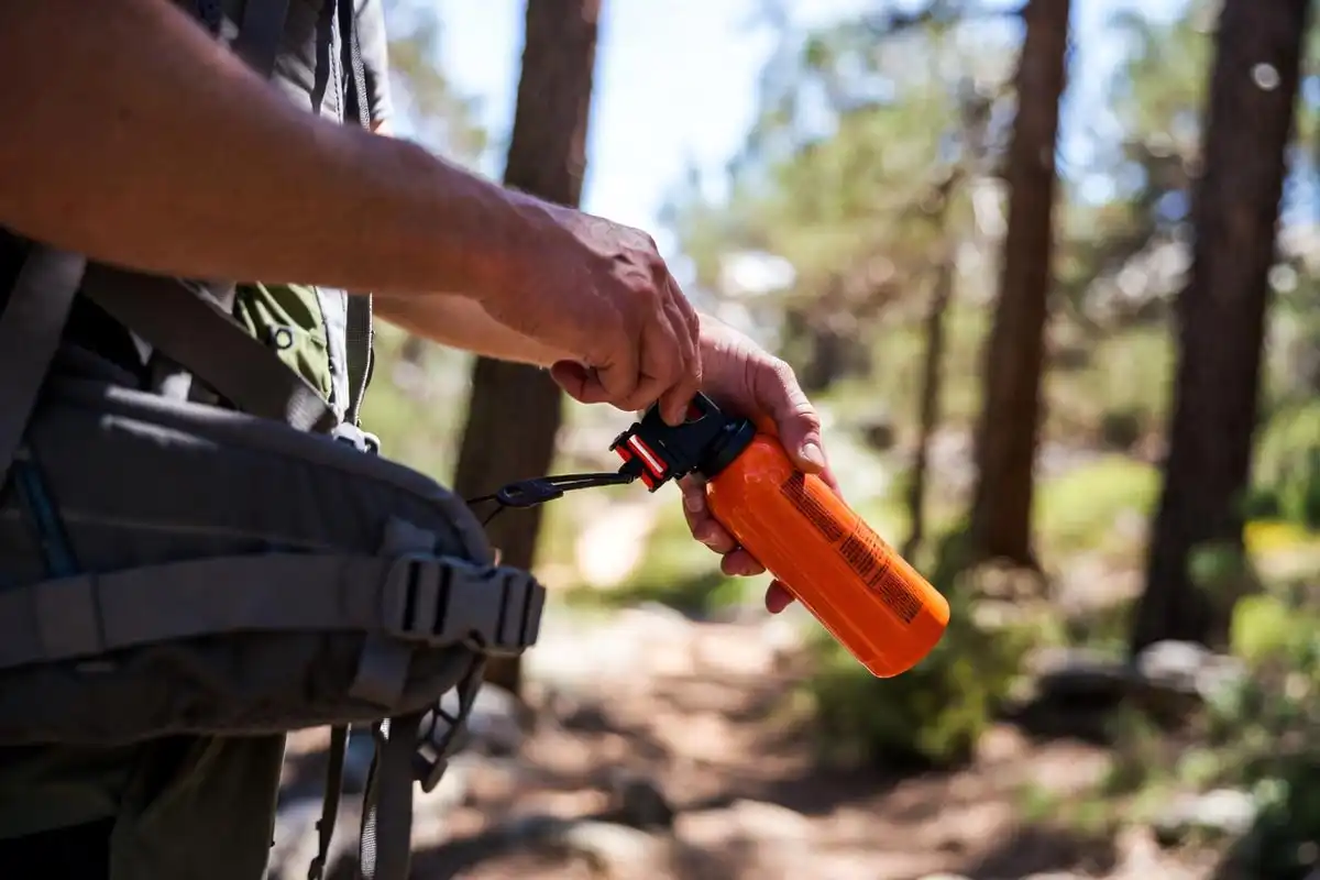 hiker clipping orange bear spray canister to backpack hip belt