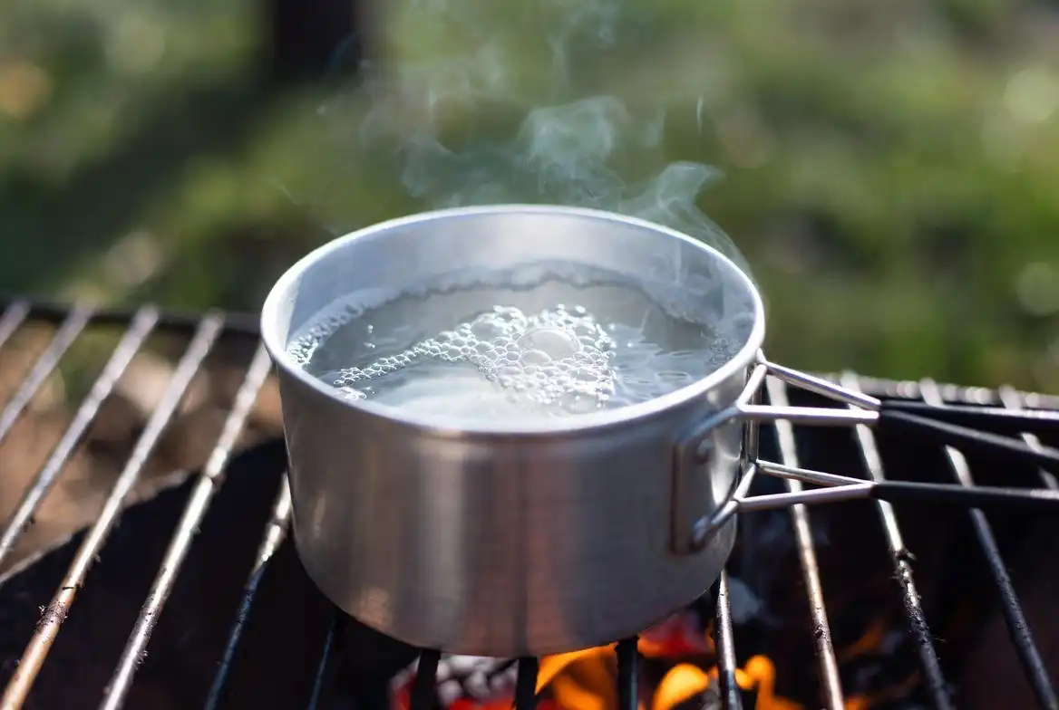 aluminum camp pot with boiling water on campfire grate over embers