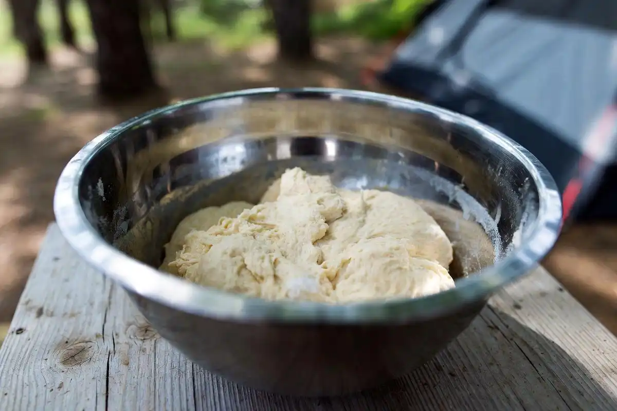 round bread dough resting in a camp bowl covered with cloth outdoors
