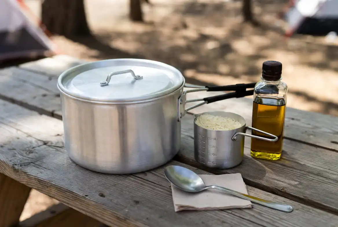 aluminum camp pot measuring cup and rice on wooden camping table
