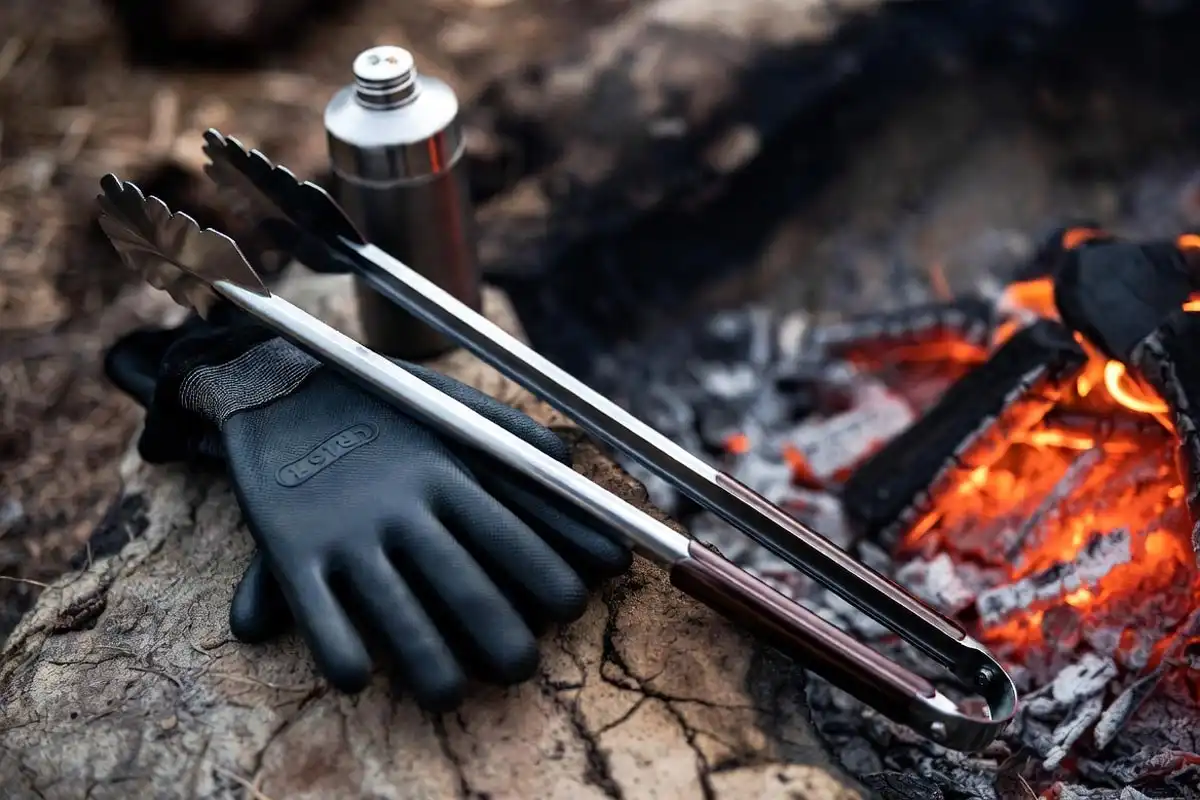 long handled tongs and heat resistant gloves beside a campfire coal bed