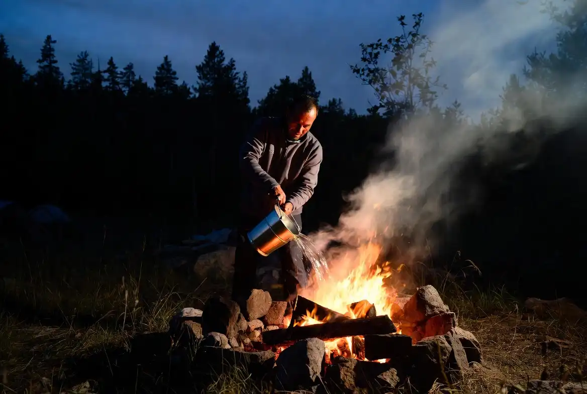 camper pouring water over campfire embers to extinguish flames safely