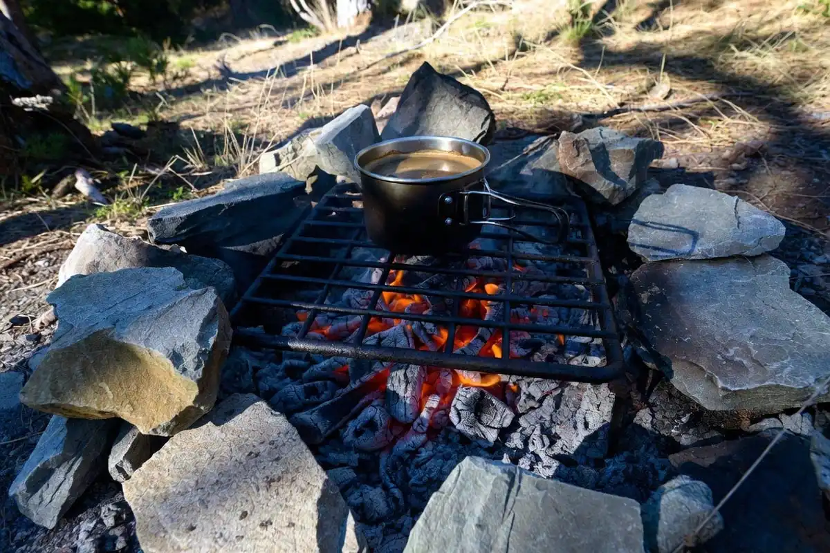 stones arranged as windbreak around campfire cooking setup in outdoor campsite