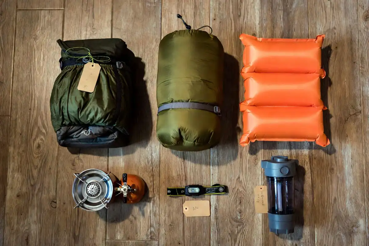 essential camping gear spread out on wooden floor with individual cost labels