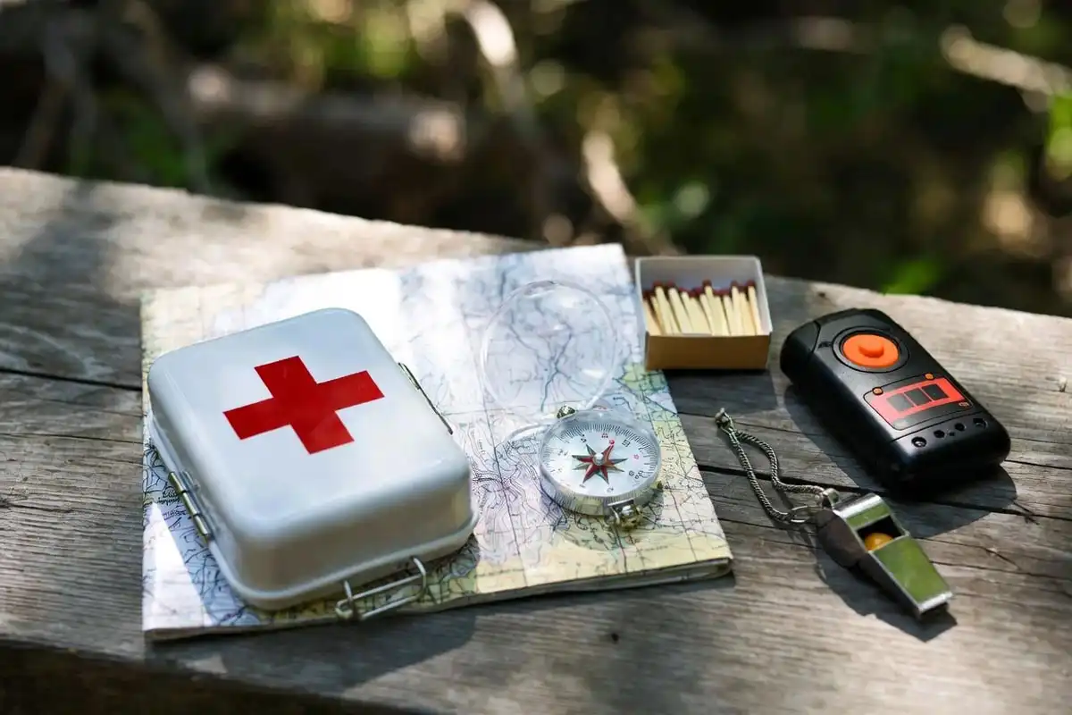 camping safety supplies including first aid kit compass map and emergency locator on wooden surface