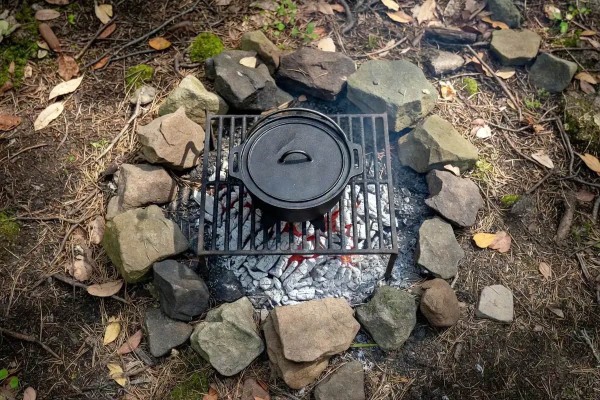 Cast iron dutch oven with legs placed on a grill grate over coals