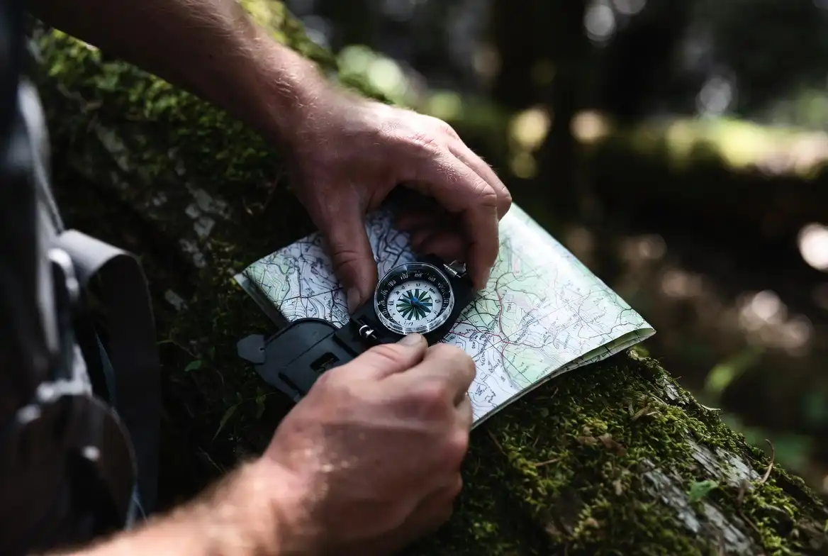 hiker's hands holding a baseplate compass over a printed topographic map on a mossy log in forest