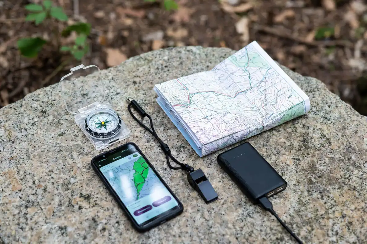 compass paper map phone and whistle arranged on granite rock for hiking