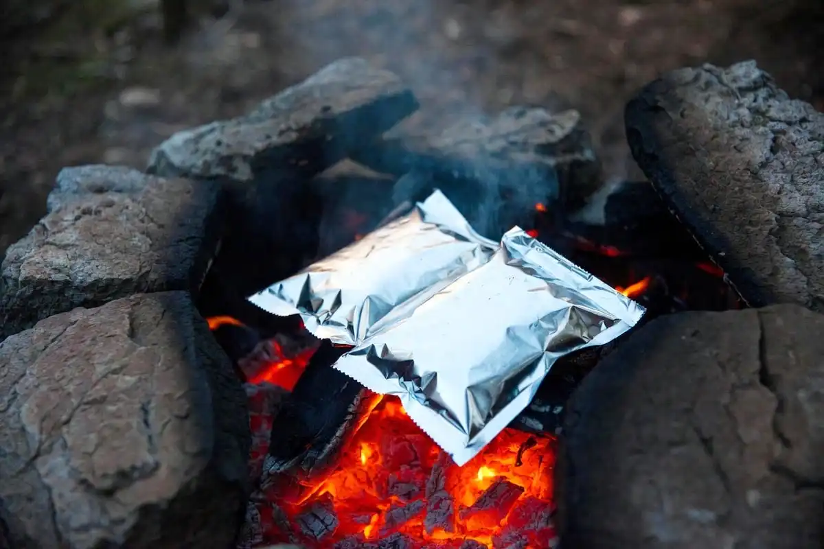 aluminum foil packet meal cooking over glowing campfire coals at night
