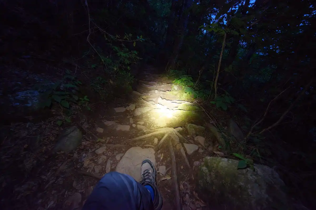 hiker directing headlamp beam toward the ground on a rocky night trail showing proper lighting angle