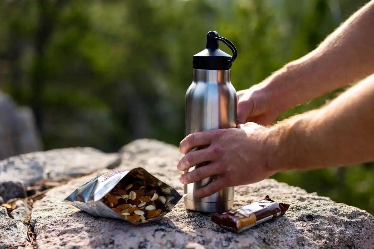 hiker drinking from water bottle next to trail snacks during a long day hike break