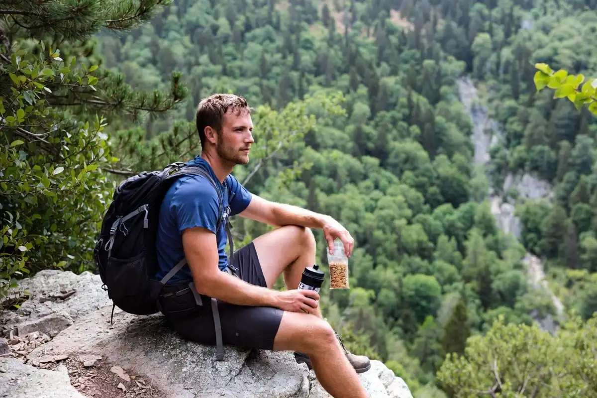hiker fueling with trail mix and water bottle during uphill rest break
