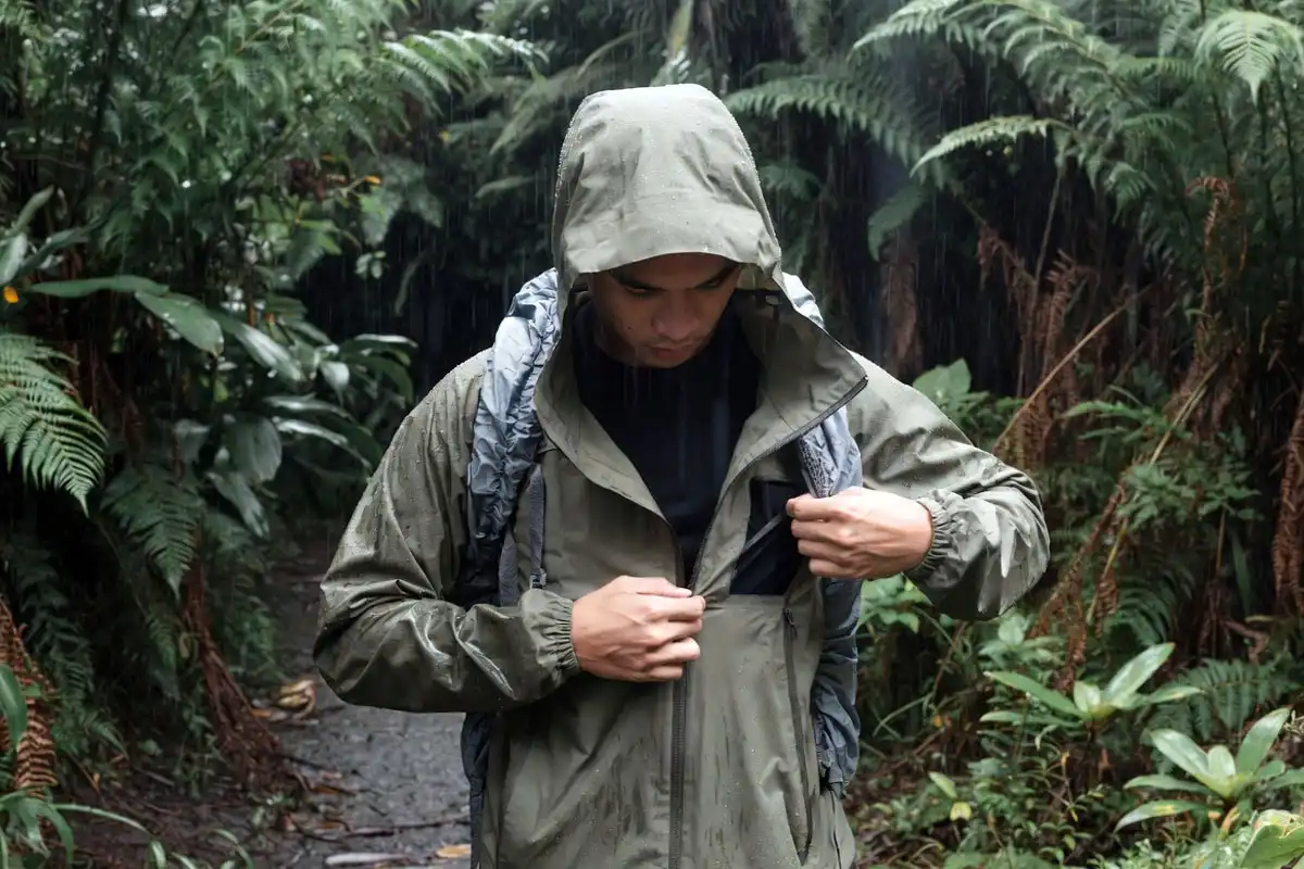 hiker adjusting pit zip on waterproof jacket during rainy trail hike