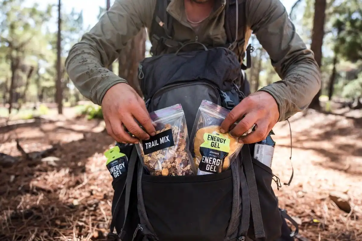 hiker placing portioned zip-lock snack bags into hip belt pocket on trail