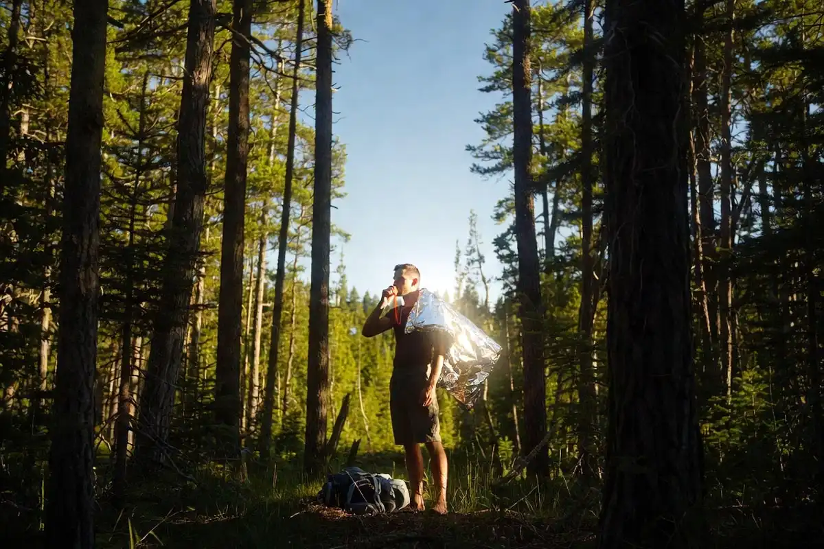 hiker blowing emergency whistle and reflecting signal mirror toward open sky in a forest clearing