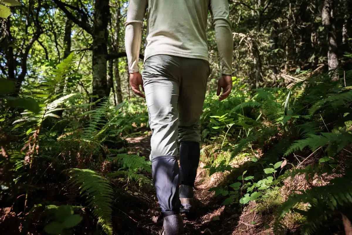 hiker in light colored long sleeve shirt with pants tucked into socks on a woodland trail