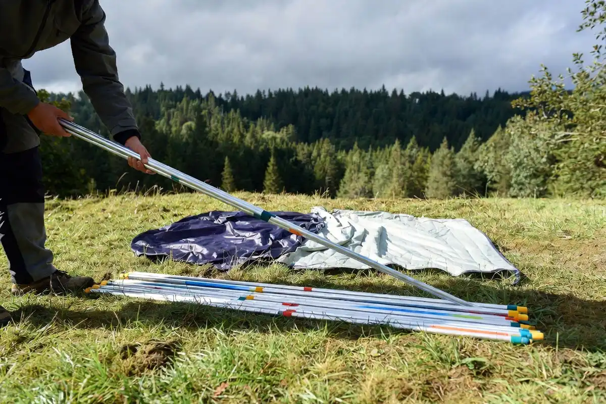 camper assembling aluminum tent poles on a flat campsite with tent body laid out