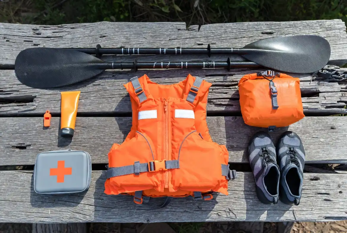 personal flotation device paddle dry bag water shoes and sunscreen laid out on a wood surface