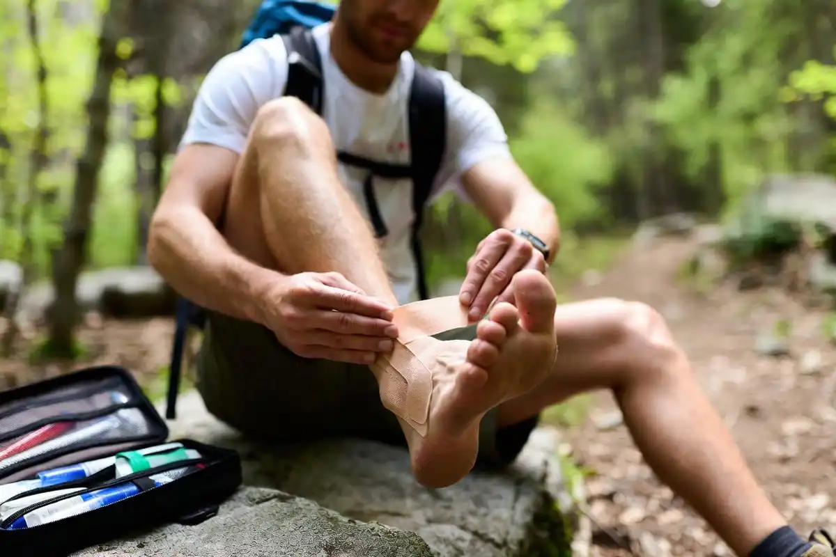 hiker applying tape to heel blister hotspot on trail