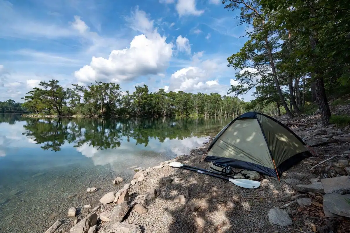 tent pitched on a gravel bank directly beside a clear freshwater lake