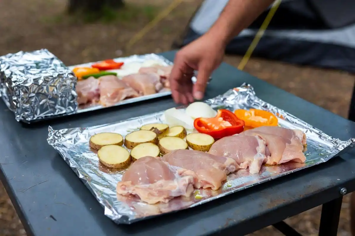 raw chicken thigh potato slices and bell pepper layered on aluminum foil ready for campfire cooking