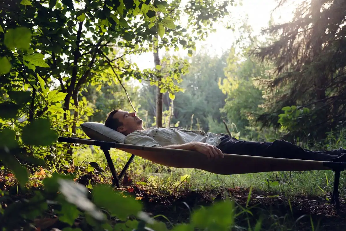 man resting on elevated camping cot at forest campsite