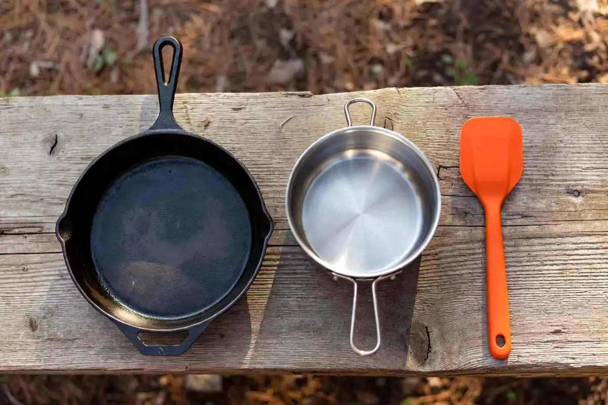 cast iron skillet pot and spatula laid out on a camp table for outdoor cooking