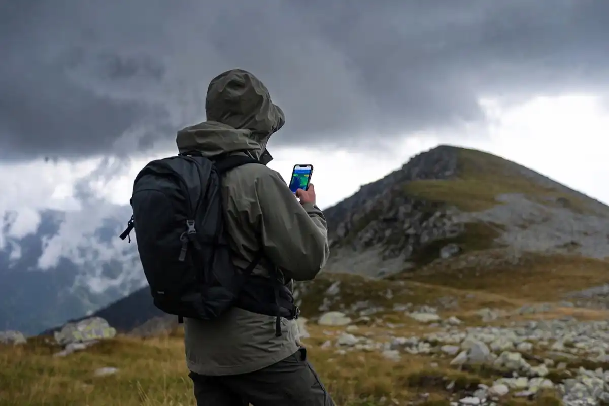 hiker checking elevation weather app on mountain ridge before storm