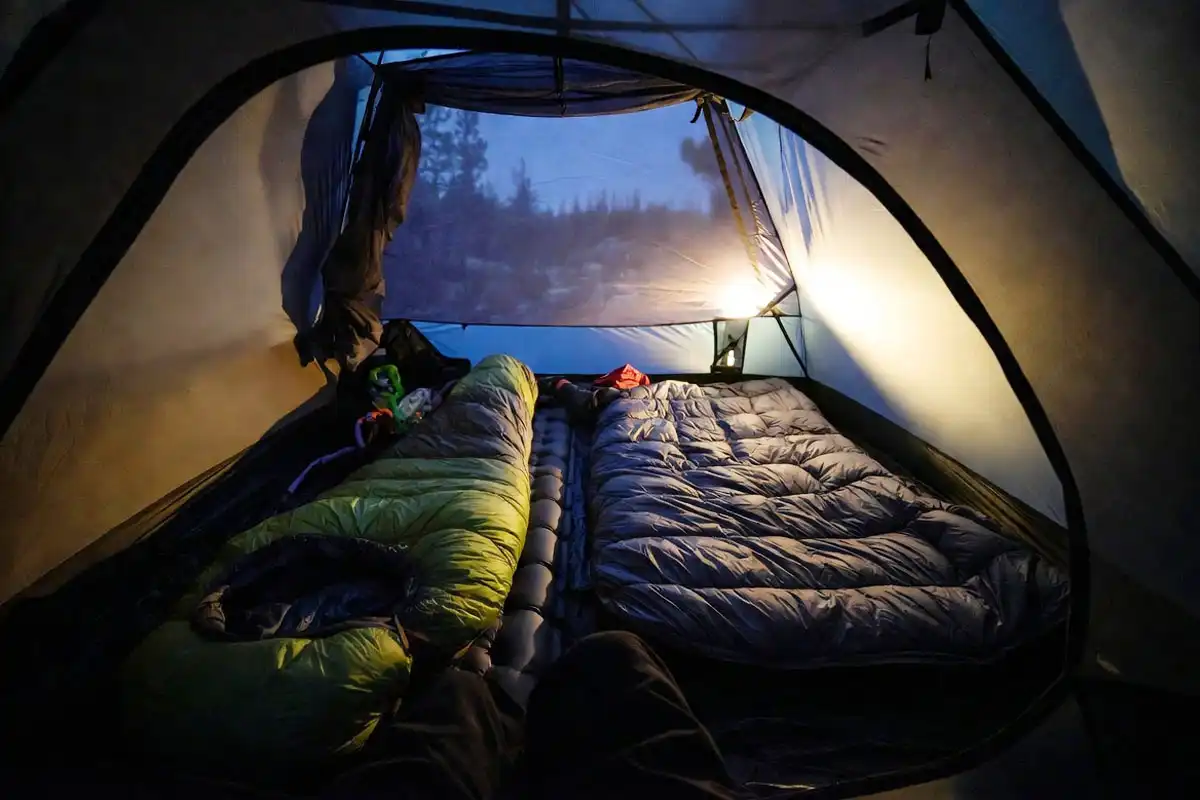 Camper comparing a zipped mummy bag and an open quilt on a tent floor