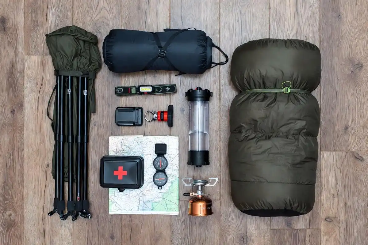 camping essentials including tent sleeping bag and headlamp arranged on wooden floor