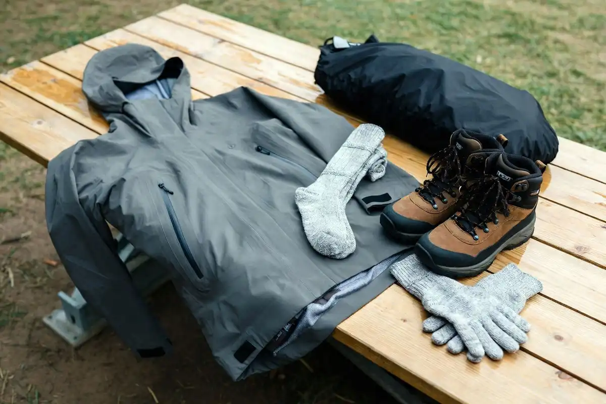 waterproof rain jacket boots and hiking gear laid flat on wooden table