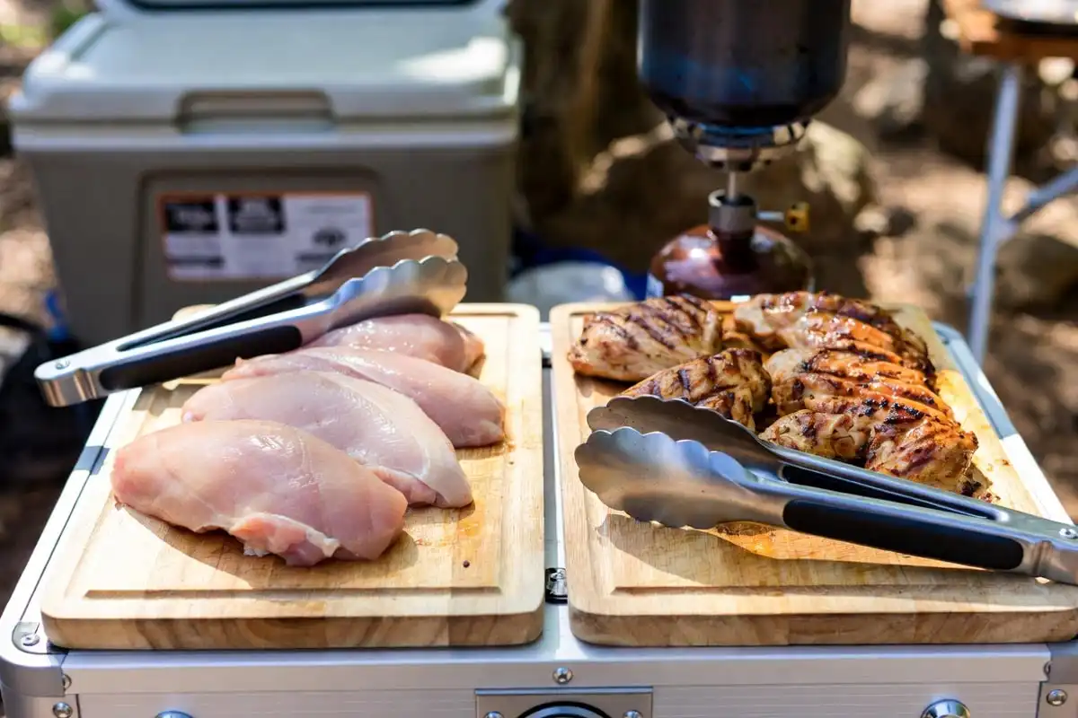 two separate cutting boards one with raw chicken one with grilled meat at campsite