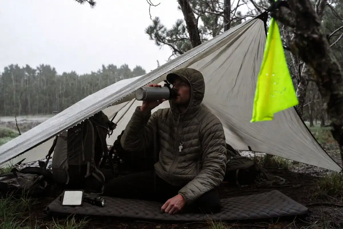 camper staying warm in a tarp shelter with signaling tools nearby