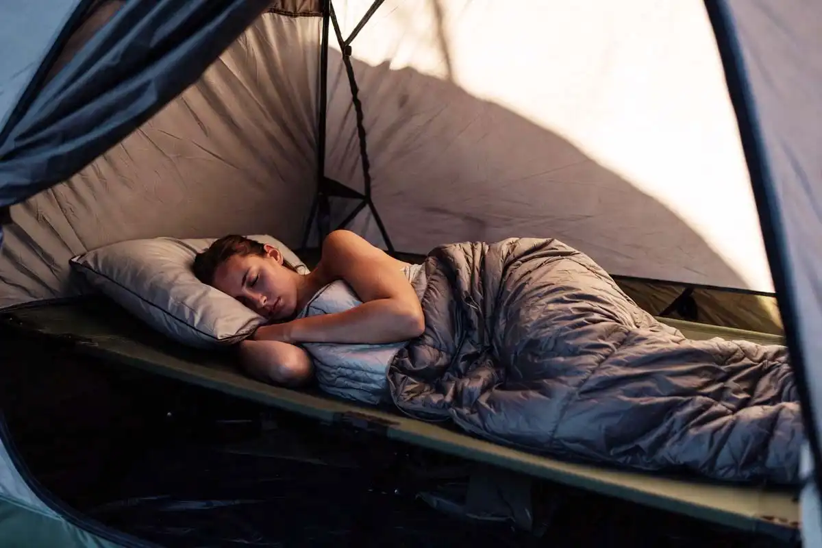 person sleeping on side on wide camp bed with knee pillow