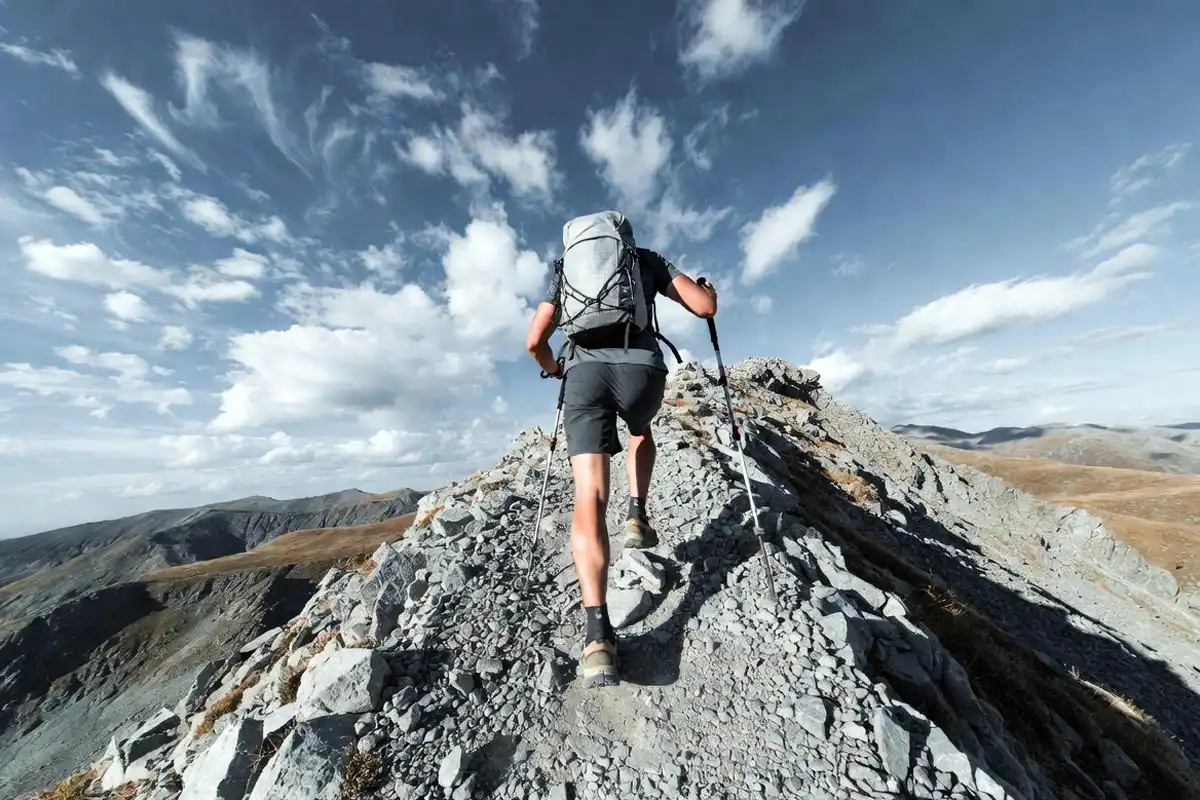 hiker with small frameless pack descending rocky mountain trail with trekking poles