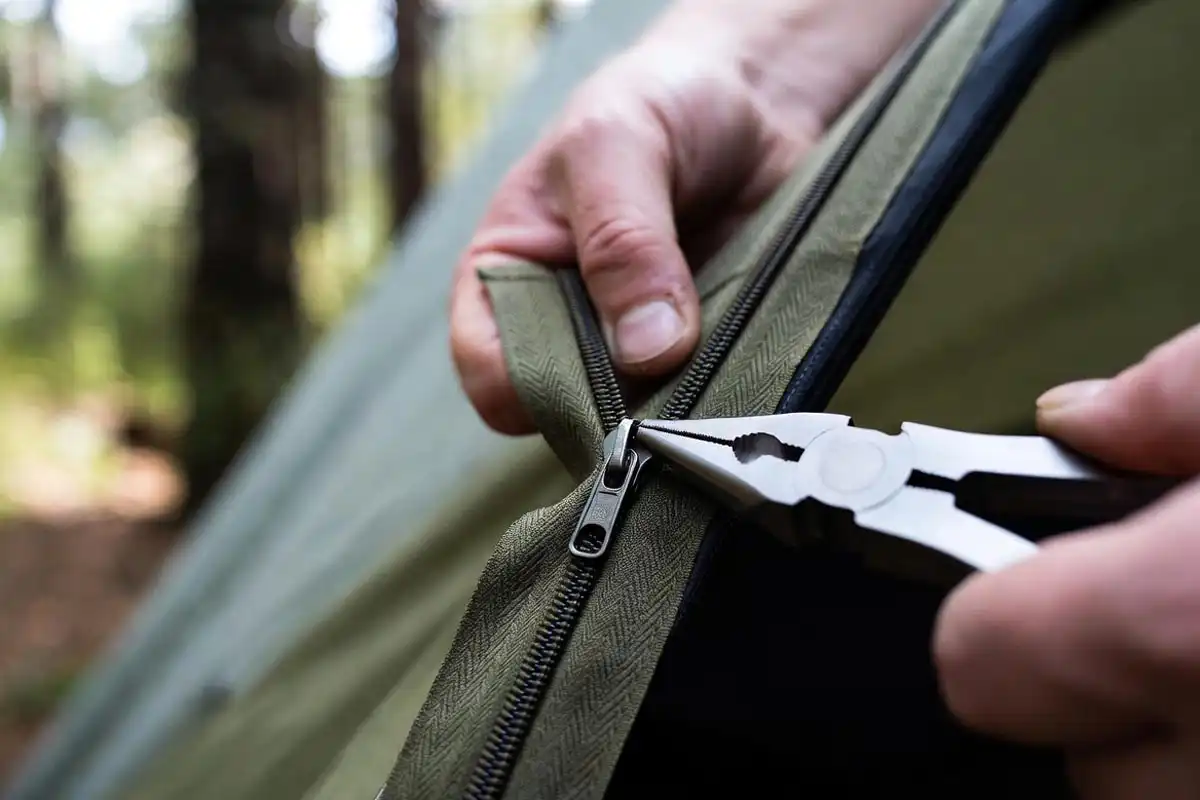 hands using needle nose pliers to gently compress a worn tent zipper slider
