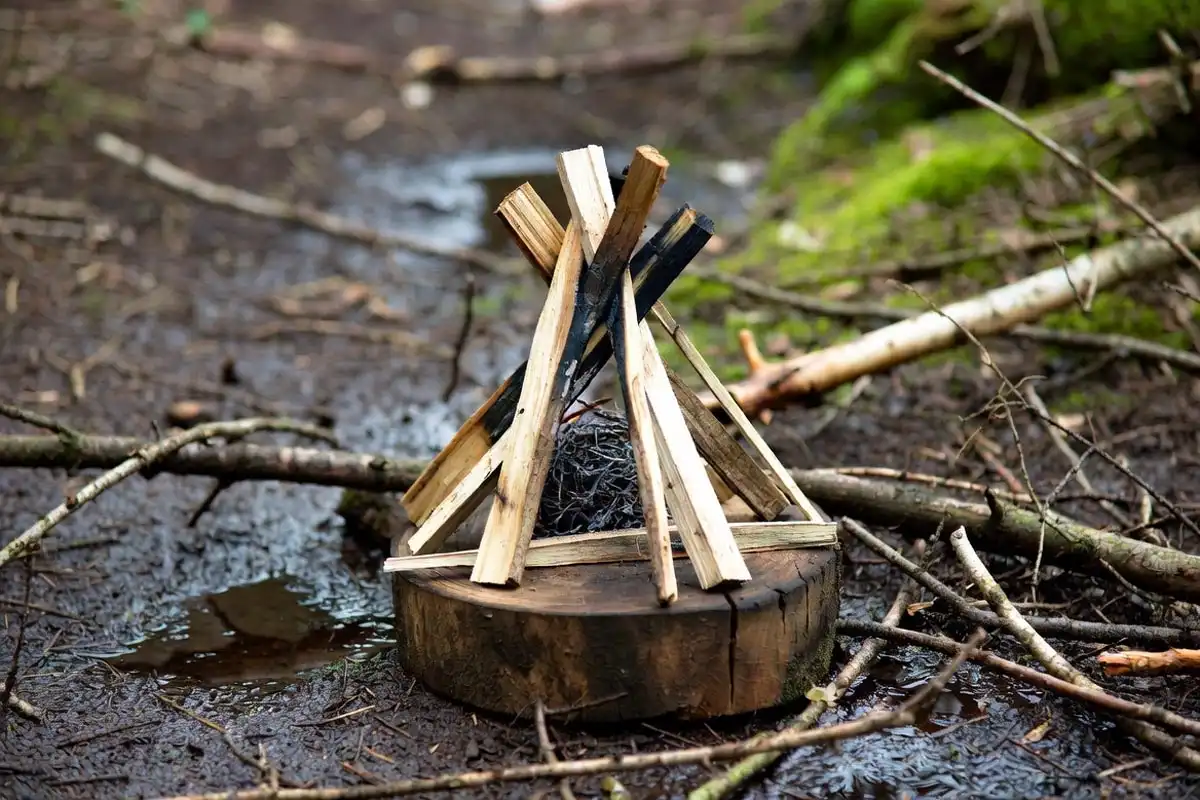 dry kindling teepee built on raised stick platform over wet soil