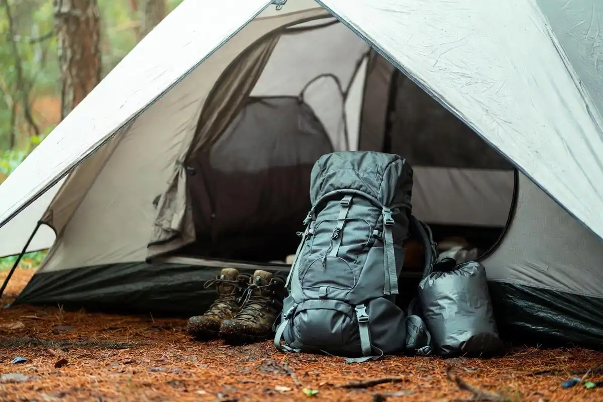 hiking boots and backpacks stored under a tent vestibule at a forest campsite