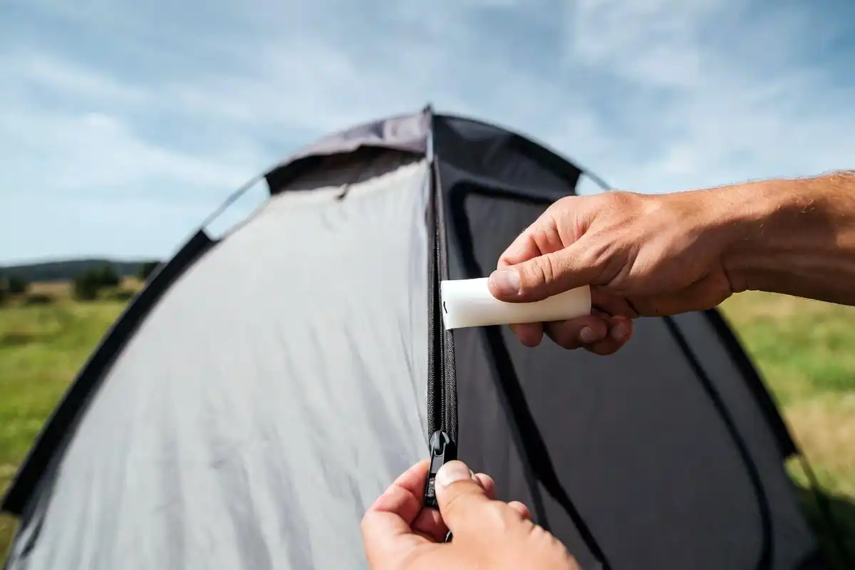 camper applying candle wax to tent zipper teeth during pre-season tent maintenance