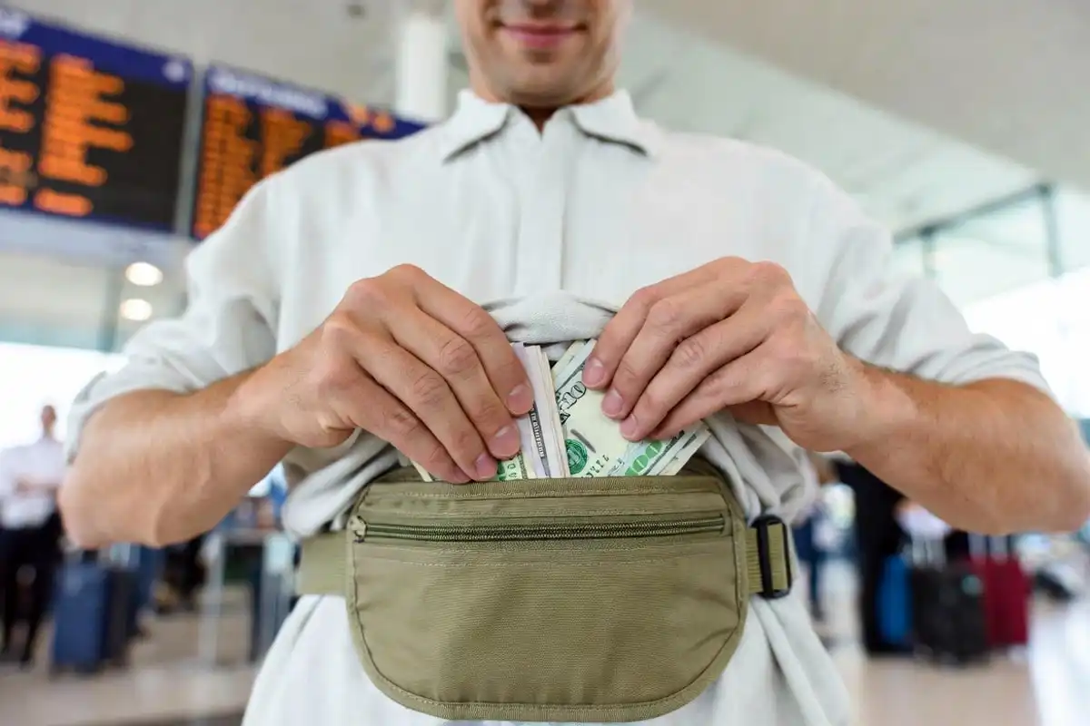 traveler placing cash into a concealed money belt under clothing at airport