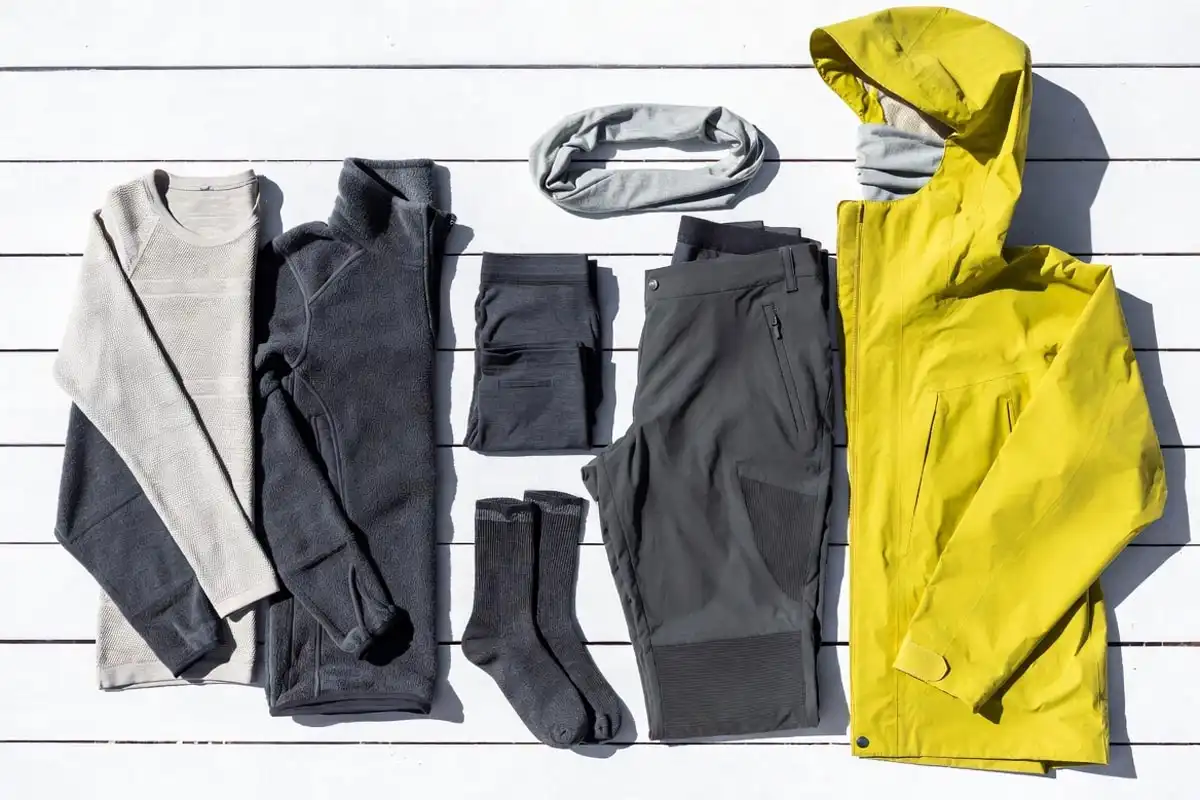merino wool shirts hiking pants rain jacket and socks laid out flat on light surface