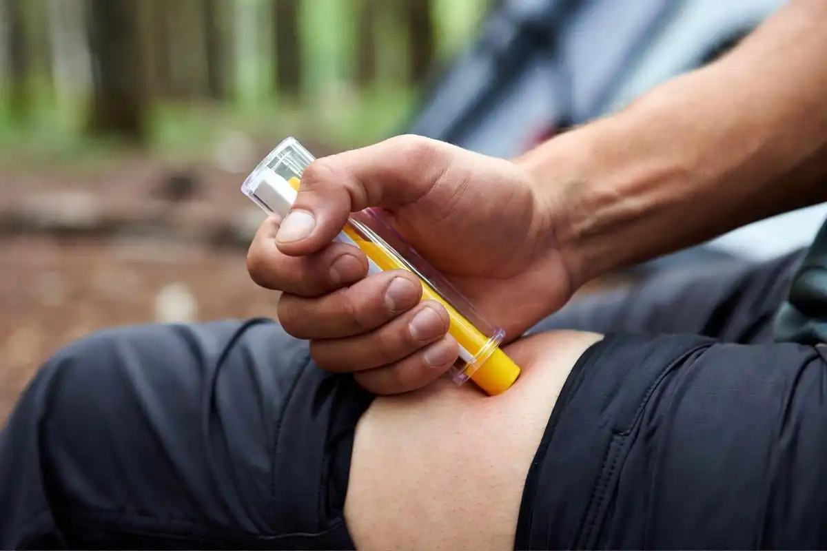 person pressing epinephrine auto injector firmly against outer thigh through clothing
