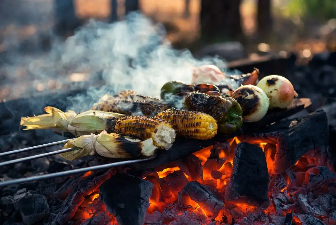 corn in husk bell peppers and whole onions roasting on hot campfire embers
