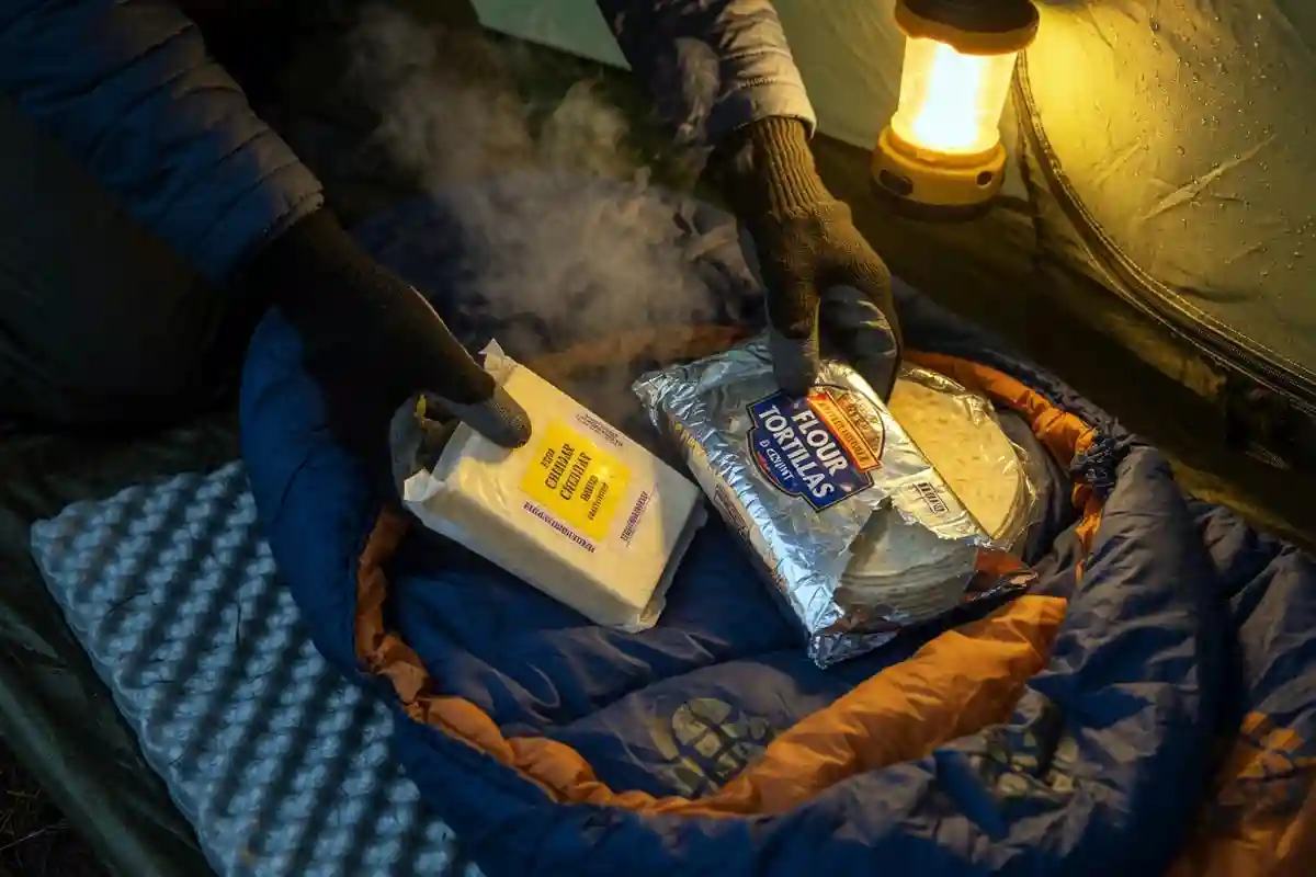 Wrapped cheese and tortillas placed inside a sleeping bag at camp