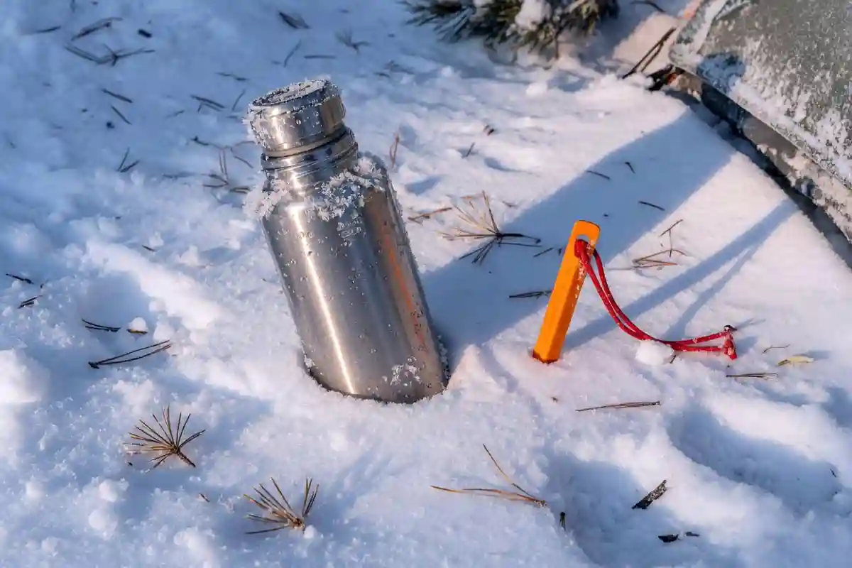 Insulated vacuum bottle stored upside down in snow near a tent